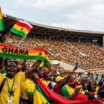 Ghana football supporters celebrating inside a packed World Cup stadium with Ghana flags and FIFA branding.