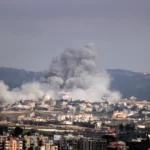 A plume of smoke rises above buildings in southern Lebanon following military exchanges as regional powers pursue ceasefire negotiations.