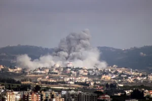 A plume of smoke rises above buildings in southern Lebanon following military exchanges as regional powers pursue ceasefire negotiations.