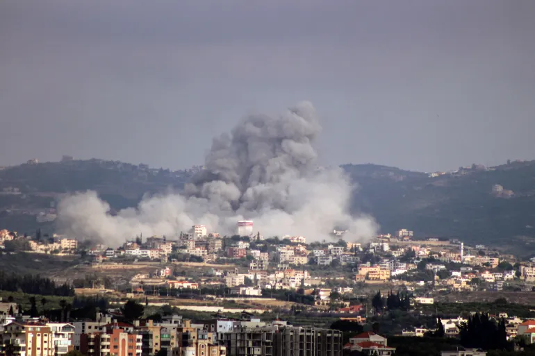 A plume of smoke rises above buildings in southern Lebanon following military exchanges as regional powers pursue ceasefire negotiations.