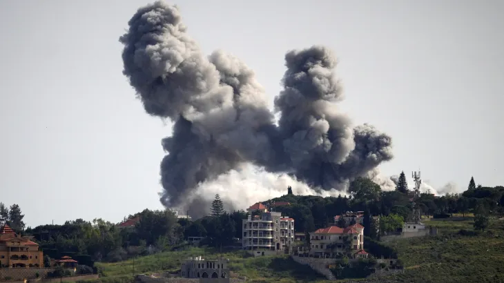 A plume of smoke rises above buildings in southern Lebanon following military exchanges as regional powers pursue ceasefire negotiations.