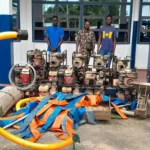 Suspects standing behind seized water pumps and equipment during an anti-galamsey operation in Ghana.