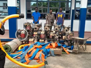 Suspects standing behind seized water pumps and equipment during an anti-galamsey operation in Ghana.