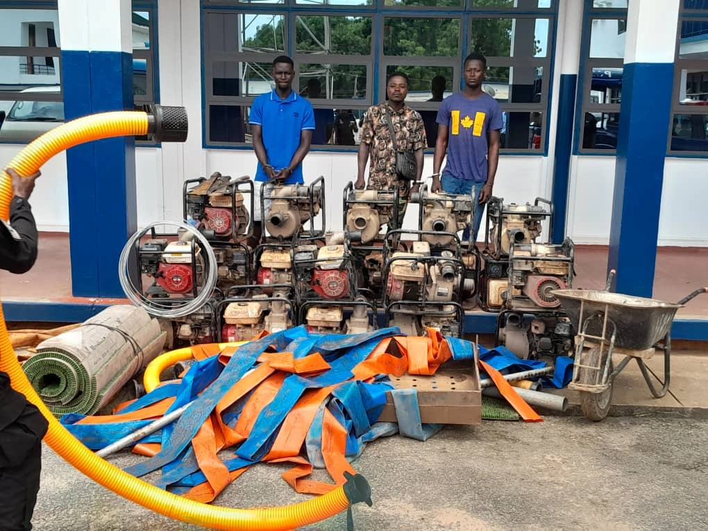 Suspects standing behind seized water pumps and equipment during an anti-galamsey operation in Ghana.