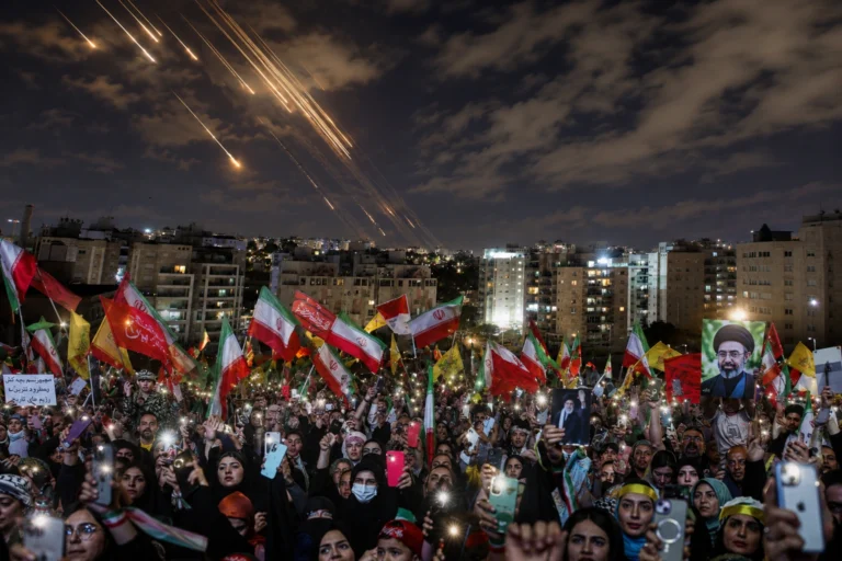 Israel Launches Strikes: Crowds waving Iranian flags gather at night as missile trails streak across the sky above a city amid escalating regional tensions.