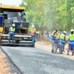 Road construction workers operate paving equipment and lay asphalt during an infrastructure development project.