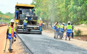 Road construction workers operate paving equipment and lay asphalt during an infrastructure development project.