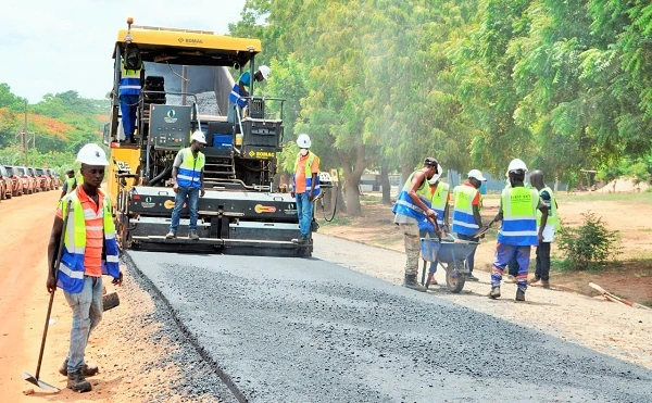 Road construction workers operate paving equipment and lay asphalt during an infrastructure development project.
