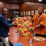 Two men present a Ghana-themed World Cup Fans Diary jersey during a meeting in a boardroom setting.