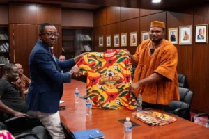 Two men present a Ghana-themed World Cup Fans Diary jersey during a meeting in a boardroom setting.